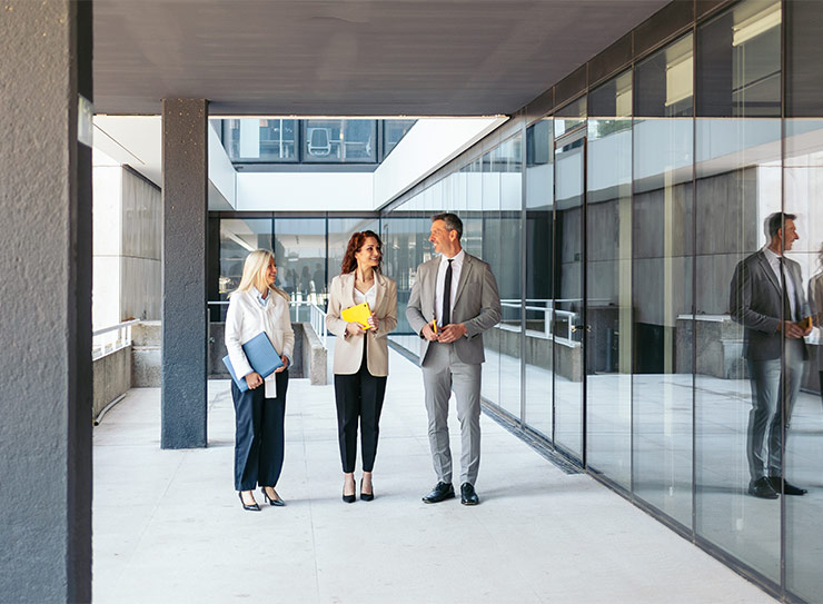 Drei Personen in Business-Kleidung gehen durch ein modernes Bürogebäude – digitale Barrierefreiheit als Nachweis der Sorgfaltspflicht und Schutz vor BFSG-Abmahnungen seit Juni 2025