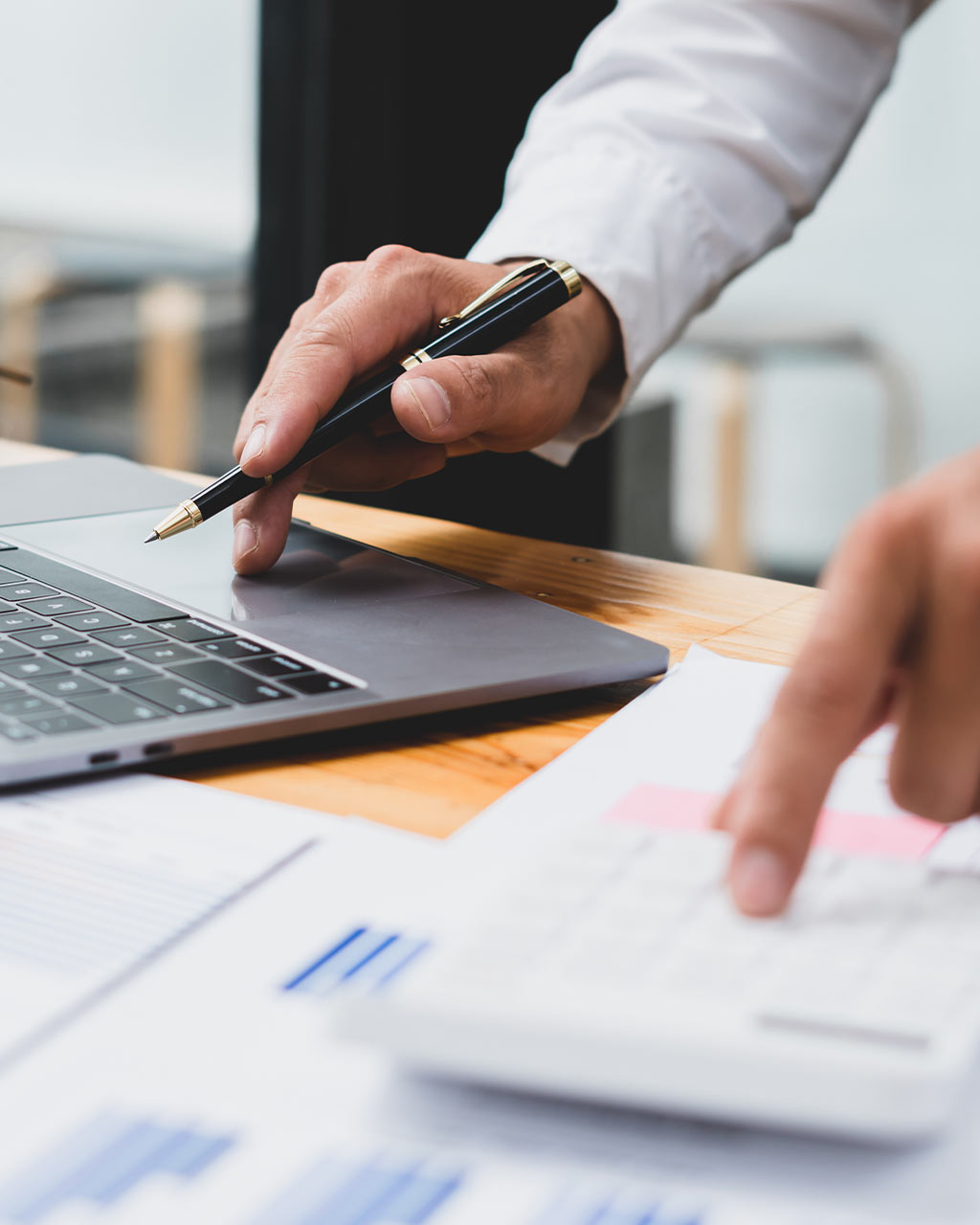 Hände arbeiten mit Stift, Taschenrechner und Finanzdokumenten neben einem Laptop – unzugängliche Antragsstrecken und Datentabellen als Barrierefreiheits-Problem für Banken und Versicherungen nach BFSG und WCAG 2.2