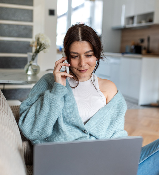 Frau sitzt auf dem Sofa, telefoniert und nutzt gleichzeitig einen Laptop – barrierefreier Self-Service für Telekommunikationsanbieter nach BFSG und WCAG 2.2