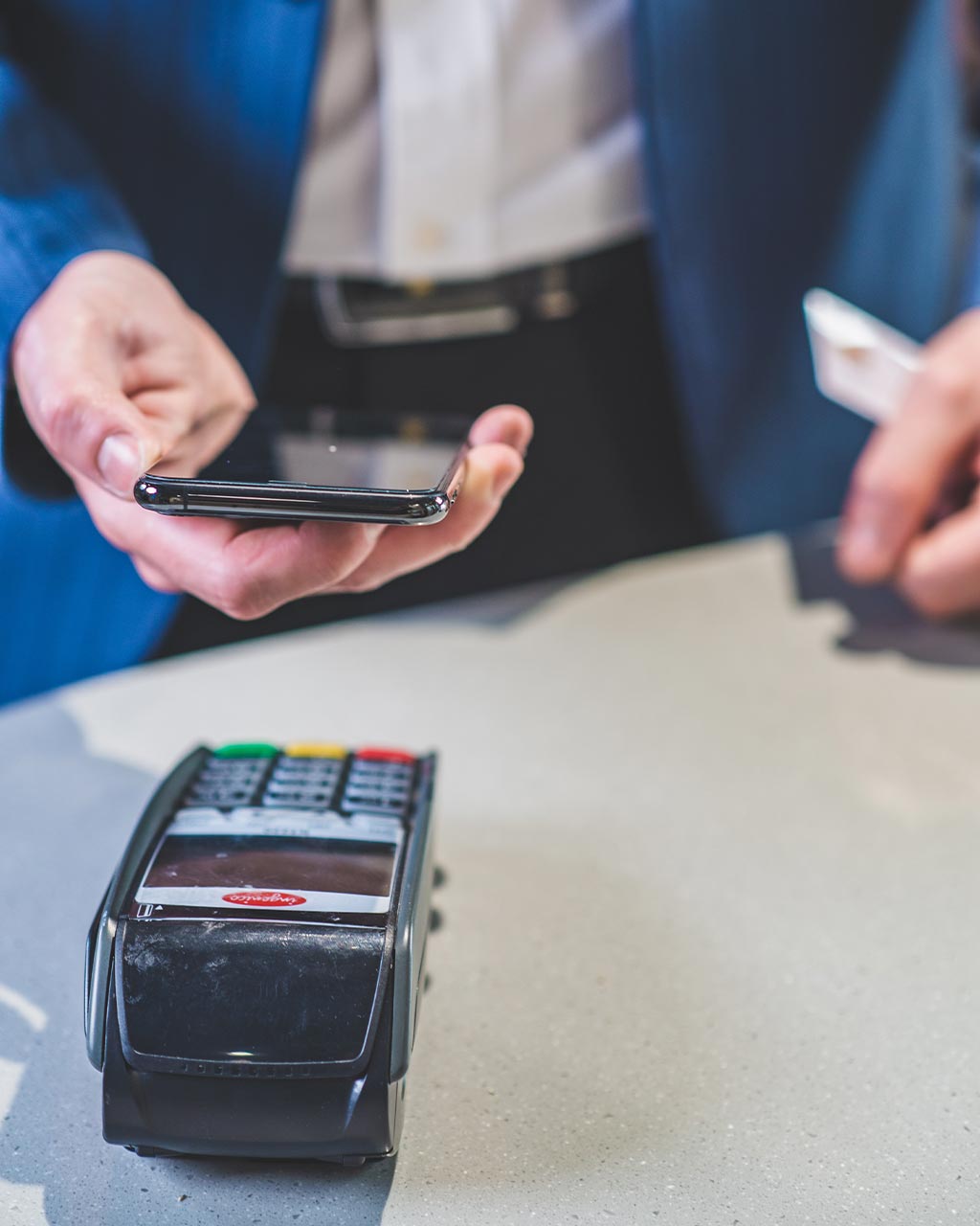 Mann im Anzug hält Smartphone an ein Kartenlesegerät beim kontaktlosen Bezahlen – unzugängliche Checkout-Prozesse und Bezahlstrecken als Barrierefreiheits-Problem für Online-Shops nach BFSG und WCAG 2.2
