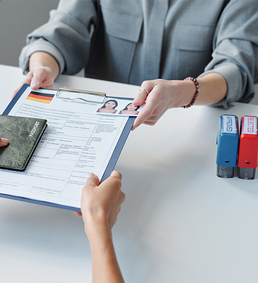 Sachbearbeiterin zeigt Bürgerin ein Behördenformular mit Reisepass auf dem Schreibtisch – barrierefreie Online-Anträge und Verwaltungsportale für Behörden nach BITV 2.0 und WCAG 2.2