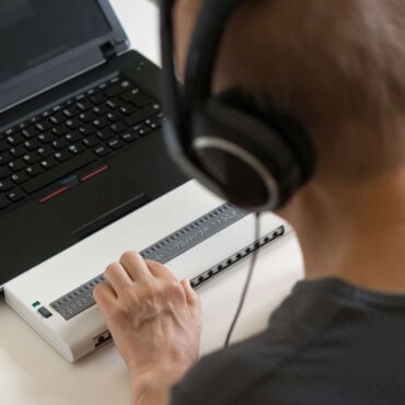 Person mit Kopfhörern bedient eine Braillezeile vor einem Laptop – Was ist ein Screenreader? Funktion, Bedeutung und Auswirkung auf die Website-Barrierefreiheit nach WCAG 2.2 und BFSG