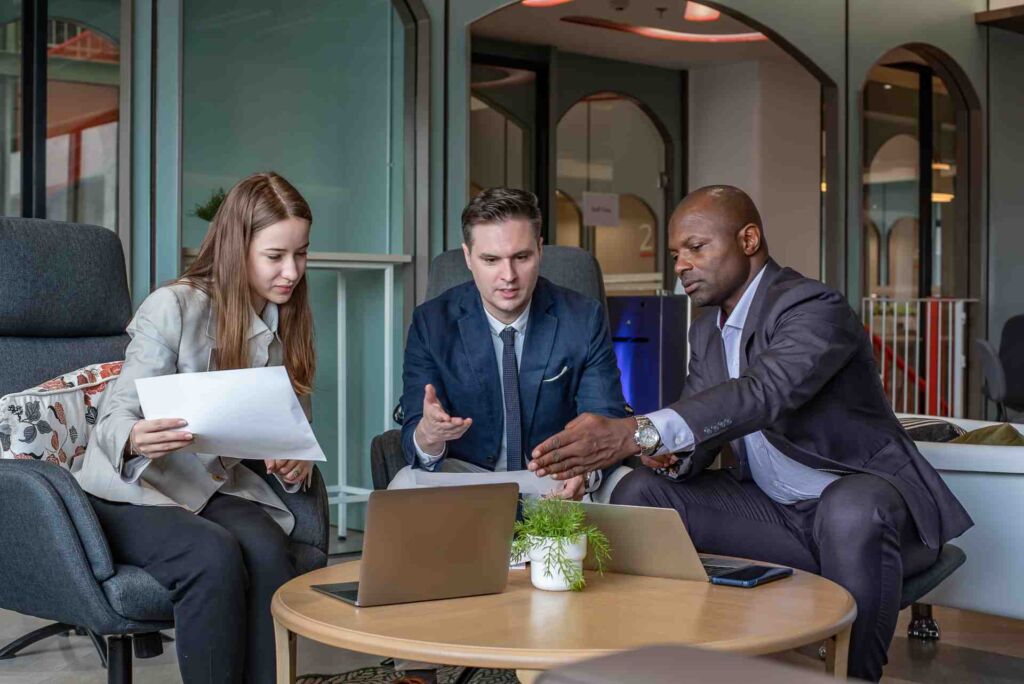 Drei Personen in Business-Kleidung besprechen ein Dokument mit Laptop – European Accessibility Act: Was der EAA und das BFSG für Unternehmen im DACH-Raum rechtlich bedeuten nach WCAG 2.2 und EN 301 549