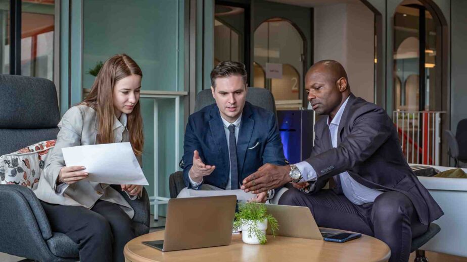Drei Personen in Business-Kleidung besprechen ein Dokument mit Laptop – European Accessibility Act: Was der EAA und das BFSG für Unternehmen im DACH-Raum rechtlich bedeuten nach WCAG 2.2 und EN 301 549