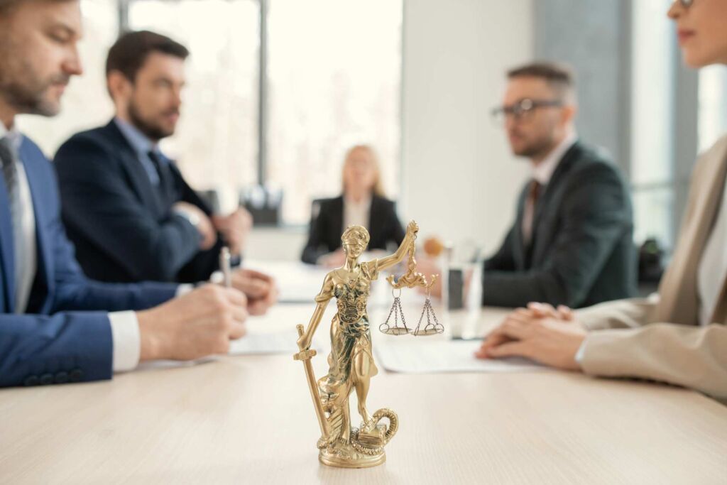 Goldene Justitia-Figur im Vordergrund eines Anwalts-Beratungsgesprächs – Abmahnung wegen fehlender Barrierefreiheit: reales BFSG-Haftungsrisiko und rechtssichere Absicherung nach WCAG 2.2