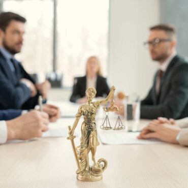 Goldene Justitia-Figur im Vordergrund eines Anwalts-Beratungsgesprächs – Abmahnung wegen fehlender Barrierefreiheit: reales BFSG-Haftungsrisiko und rechtssichere Absicherung nach WCAG 2.2