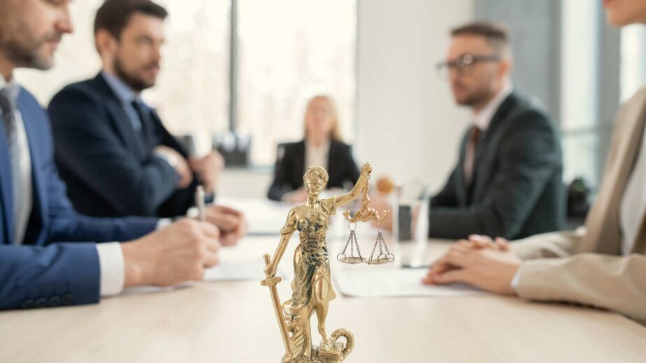 Goldene Justitia-Figur im Vordergrund eines Anwalts-Beratungsgesprächs – Abmahnung wegen fehlender Barrierefreiheit: reales BFSG-Haftungsrisiko und rechtssichere Absicherung nach WCAG 2.2