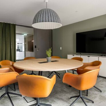 Moderner Konferenzraum mit rundem Holztisch und orangen Designerstühlen – Beratungsstandort der IFDB GmbH für digitale Barrierefreiheit und BFSG-Compliance in München
