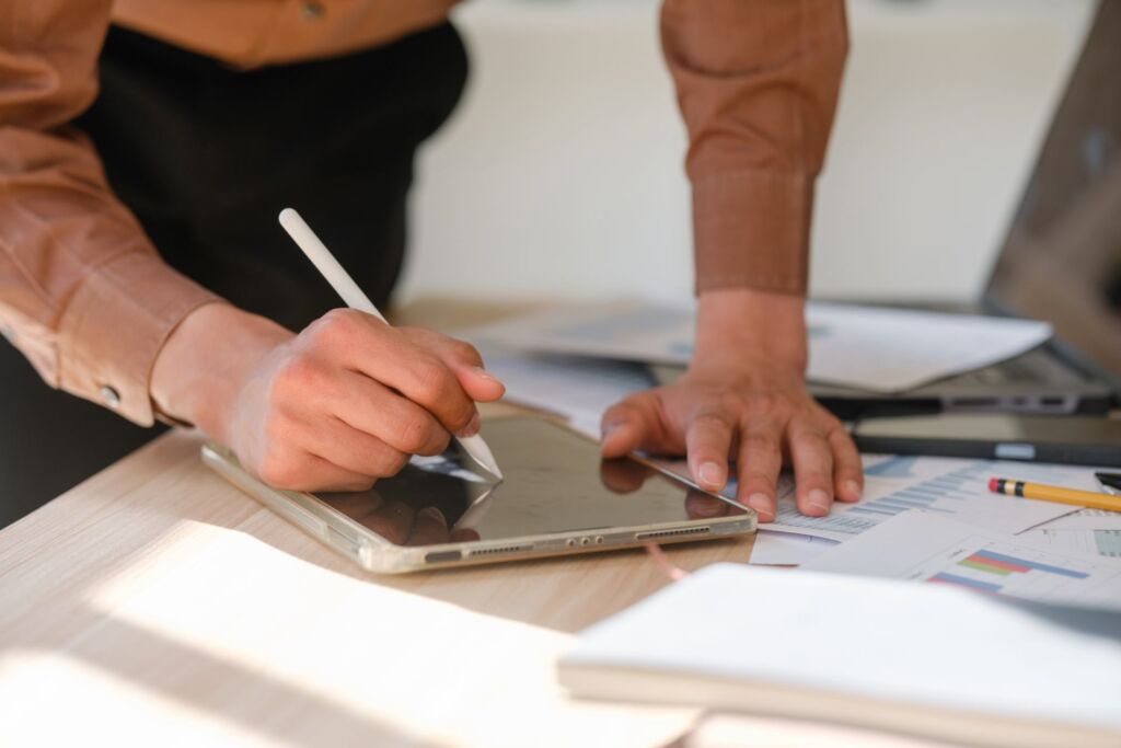 Person arbeitet mit Stylus auf einem Tablet neben Checklisten und Auswertungsunterlagen – Barrierefreiheit testen: Methoden, Tools und Checkliste für den Einstieg nach WCAG 2.2 und BFSG