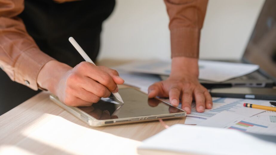 Person arbeitet mit Stylus auf einem Tablet neben Checklisten und Auswertungsunterlagen – Barrierefreiheit testen: Methoden, Tools und Checkliste für den Einstieg nach WCAG 2.2 und BFSG
