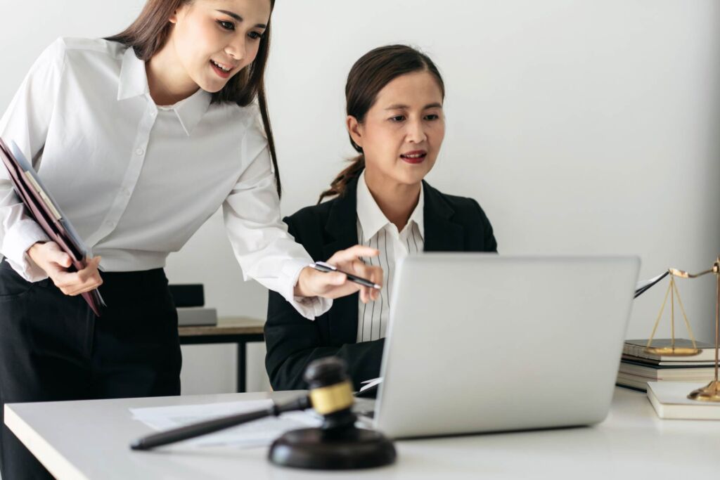 Zwei Frauen arbeiten gemeinsam am Laptop, im Vordergrund Richterhammer und Justitia-Waage – barrierefreie Formulare gestalten: Labels, Fehlermeldungen und Validierung nach WCAG 2.2 und BFSG