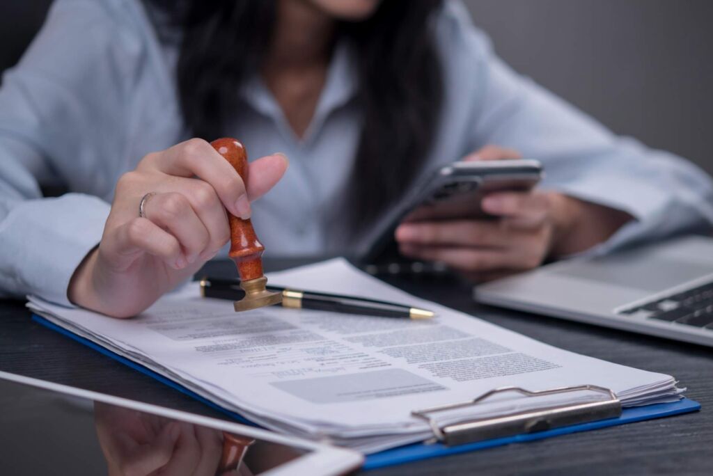 Hand setzt einen Stempel auf ein offizielles Dokument neben Smartphone und Laptop – Barrierefreiheit zertifizieren lassen: Was ein belastbarer BFSG-Nachweis nach WCAG 2.2 können muss