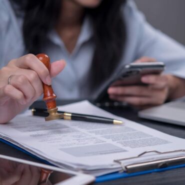 Hand setzt einen Stempel auf ein offizielles Dokument neben Smartphone und Laptop – Barrierefreiheit zertifizieren lassen: Was ein belastbarer BFSG-Nachweis nach WCAG 2.2 können muss