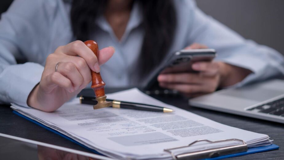 Hand setzt einen Stempel auf ein offizielles Dokument neben Smartphone und Laptop – Barrierefreiheit zertifizieren lassen: Was ein belastbarer BFSG-Nachweis nach WCAG 2.2 können muss