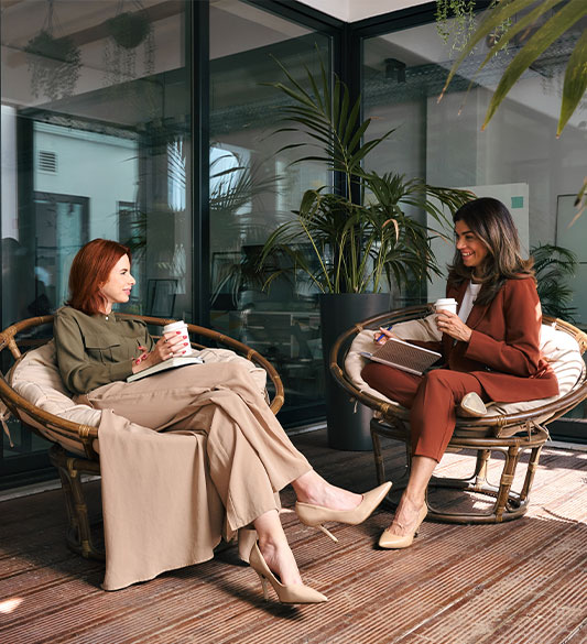 Zwei Frauen sitzen entspannt mit Kaffee auf einer Terrasse im lockeren Austausch – partnerschaftliche Zusammenarbeit mit IFDB als White-Label-Partner für digitale Barrierefreiheit nach BFSG