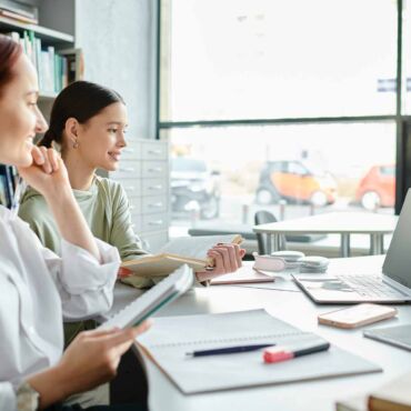 Zwei Frauen arbeiten konzentriert mit Unterlagen und Laptop am Tisch – Erklärung zur Barrierefreiheit: Pflichtinhalte, Aufbau und häufige Fehler bei der BFSG- und BITV-2.0-konformen Konformitätserklärung