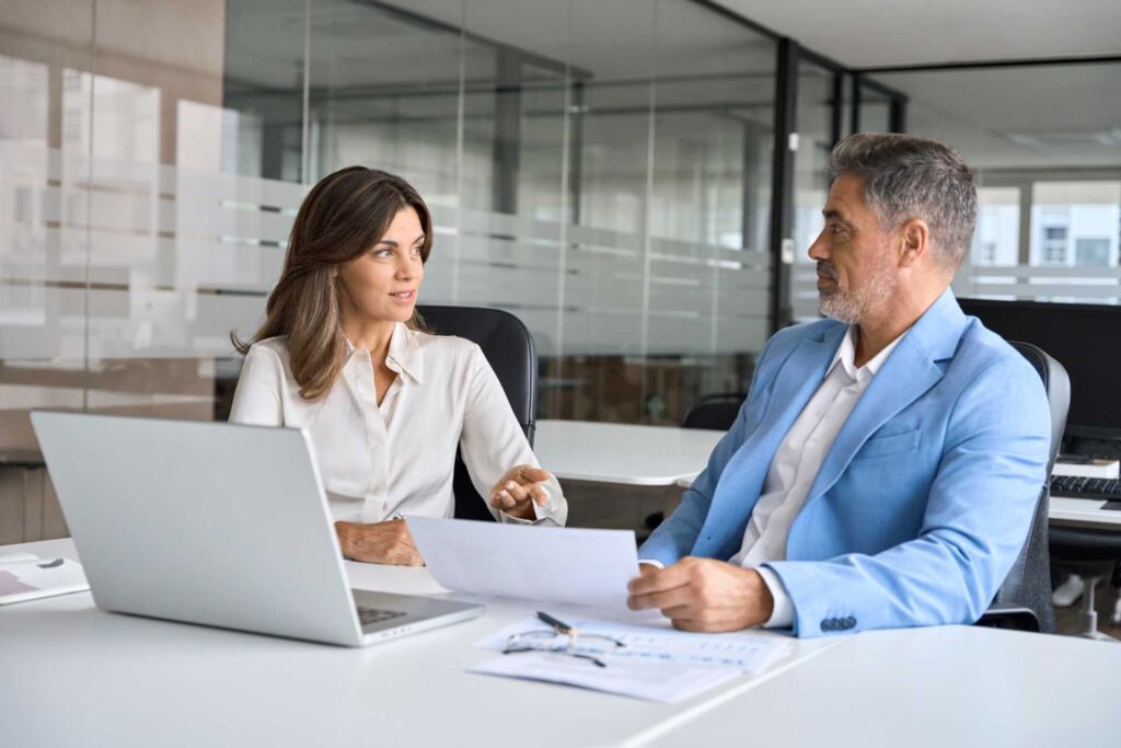 Zwei Personen im professionellen Beratungsgespräch mit Dokument und Laptop – EN 301 549: die technische Norm hinter BFSG und BITV 2.0 verstehen und in der Praxis anwenden nach WCAG 2.2