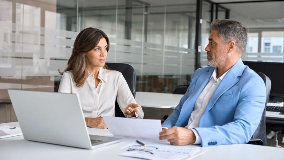 Zwei Personen im professionellen Beratungsgespräch mit Dokument und Laptop – EN 301 549: die technische Norm hinter BFSG und BITV 2.0 verstehen und in der Praxis anwenden nach WCAG 2.2