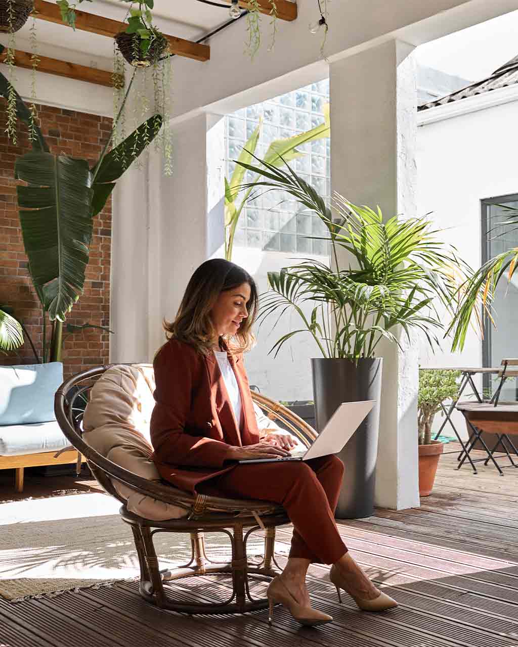 Frau im roten Businessanzug arbeitet konzentriert auf einem Laptop auf einer begrünten Terrasse – skalierbare PDF-Remediation für Behörden, Konzerne und Online-Händler nach BFSG, BITV 2.0 und PDF/UA