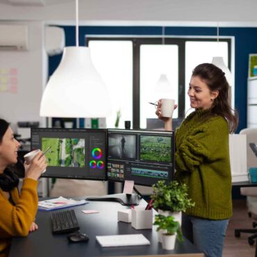 Zwei Designerinnen im lockeren Austausch vor einem Multi-Monitor-Setup mit Grafikbearbeitungssoftware – barrierefreies Webdesign: Prinzipien für kontrastreiche, tastaturzugängliche und screenreaderkompatible Websites nach WCAG 2.2