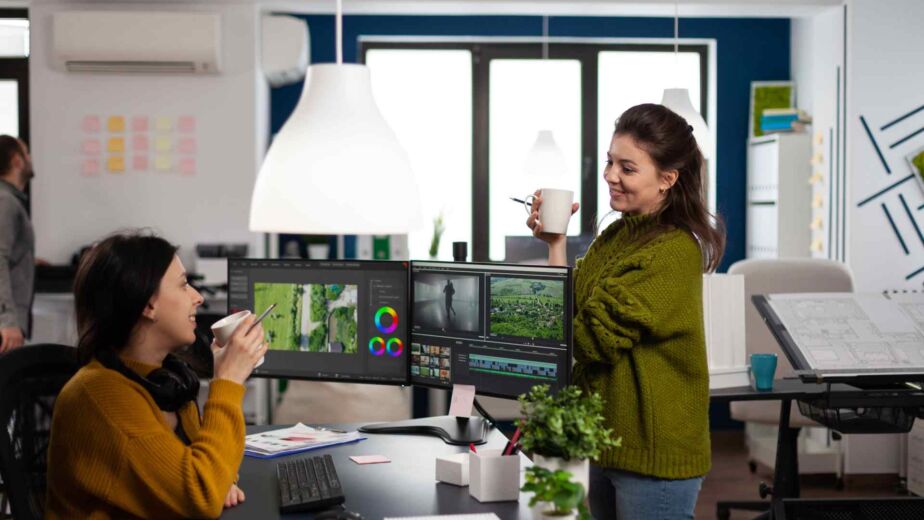 Zwei Designerinnen im lockeren Austausch vor einem Multi-Monitor-Setup mit Grafikbearbeitungssoftware – barrierefreies Webdesign: Prinzipien für kontrastreiche, tastaturzugängliche und screenreaderkompatible Websites nach WCAG 2.2