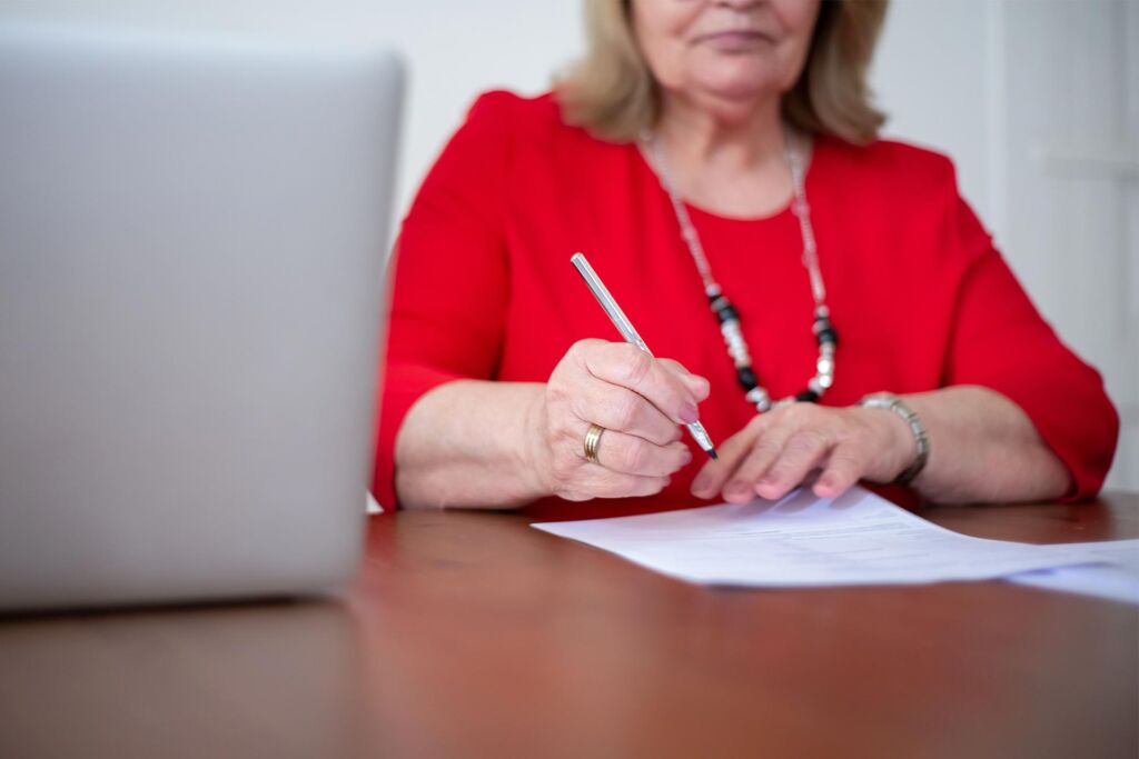 Frau unterschreibt Dokument neben geöffnetem Laptop – Barrierefreiheitserklärung Pflicht und Inhalt nach BFSG
