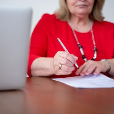 Frau unterschreibt Dokument neben geöffnetem Laptop – Barrierefreiheitserklärung Pflicht und Inhalt nach BFSG