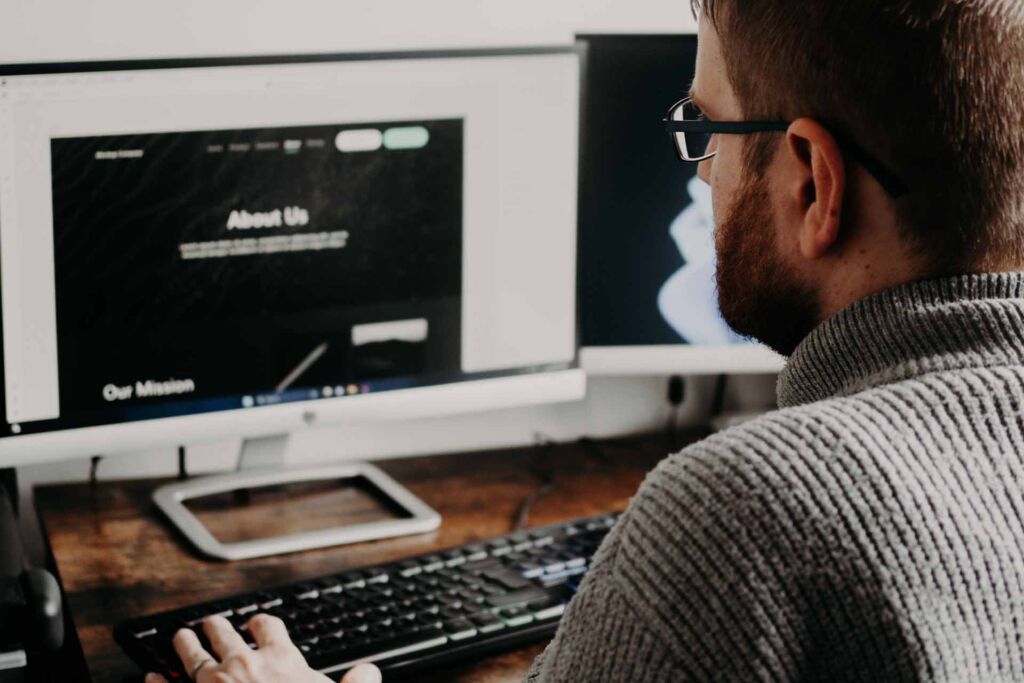 Mann prüft Website mit Überschriften 'About Us' und 'Our Mission' – barrierefreie Überschriftenstruktur als Landkarte der Seite
