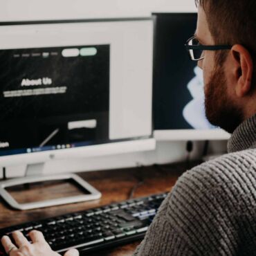 Mann prüft Website mit Überschriften 'About Us' und 'Our Mission' – barrierefreie Überschriftenstruktur als Landkarte der Seite