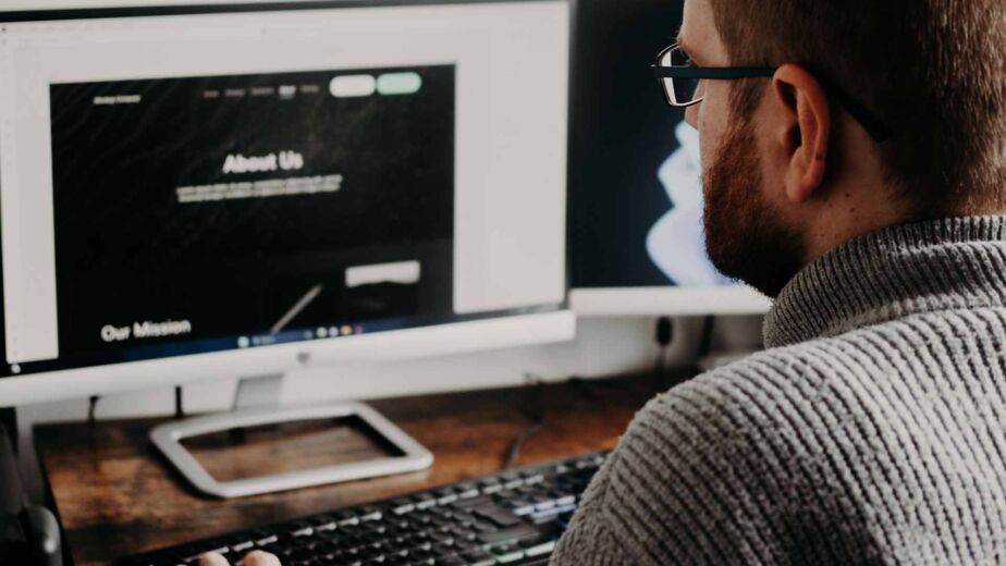 Mann prüft Website mit Überschriften 'About Us' und 'Our Mission' – barrierefreie Überschriftenstruktur als Landkarte der Seite