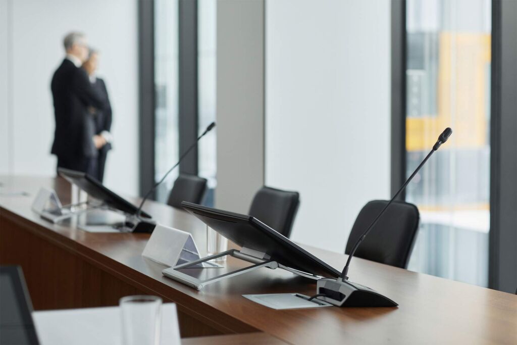 Konferenztisch mit Rednermikrofonen in Behördensaal – BGG, BITV, BFSG und EAA im Gesetzes-Überblick