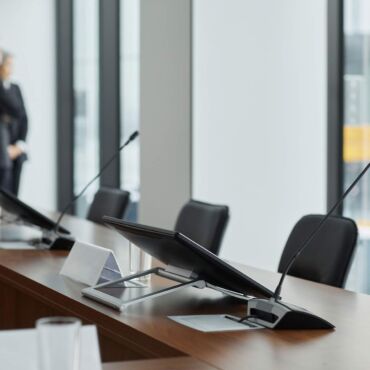 Konferenztisch mit Rednermikrofonen in Behördensaal – BGG, BITV, BFSG und EAA im Gesetzes-Überblick