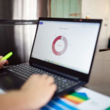 Person zeigt auf Ringdiagramm am Laptop neben bunten Balkengrafiken – Barrierefreiheits-Test: Tools im Vergleich