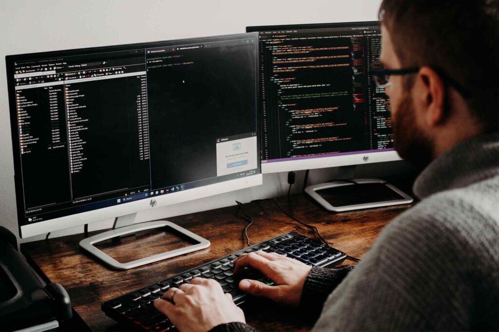 Programmierer arbeitet an zwei Bildschirmen mit Quellcode – barrierefreies Webdesign im Entwicklungsprozess