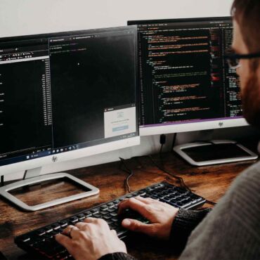 Programmierer arbeitet an zwei Bildschirmen mit Quellcode – barrierefreies Webdesign im Entwicklungsprozess