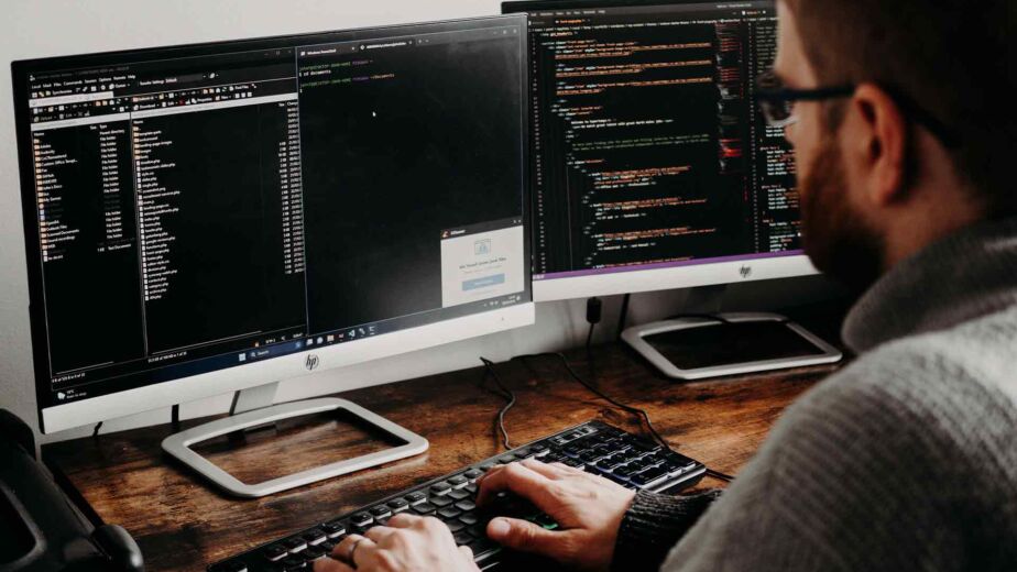 Programmierer arbeitet an zwei Bildschirmen mit Quellcode – barrierefreies Webdesign im Entwicklungsprozess