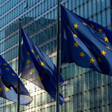EU-Flaggen wehen vor Glasgebäude – European Accessibility Act: der EU-Rahmen für Barrierefreiheit