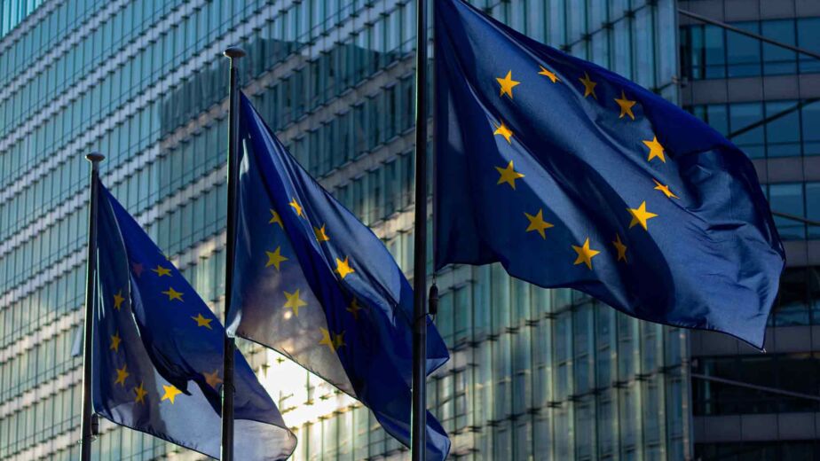 EU-Flaggen wehen vor Glasgebäude – European Accessibility Act: der EU-Rahmen für Barrierefreiheit