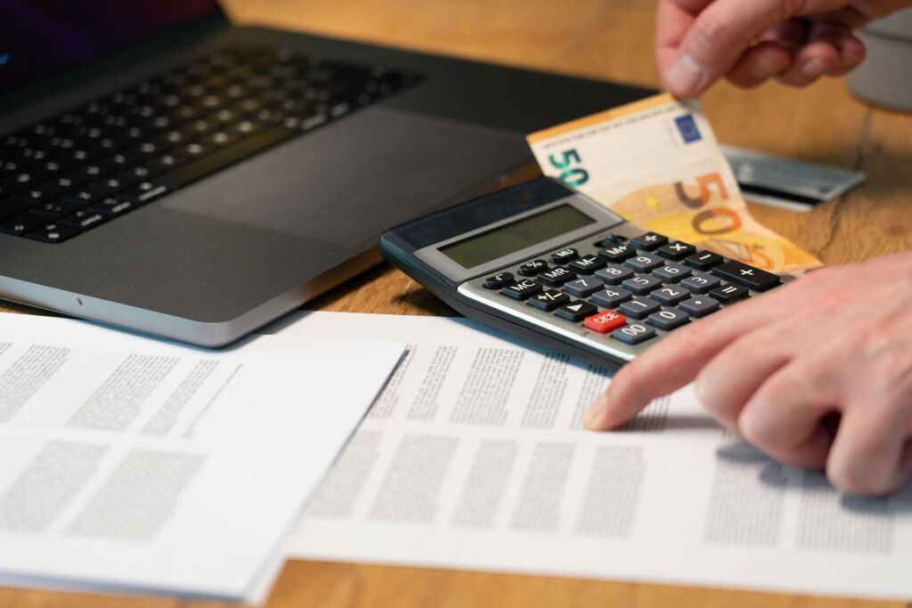 Hand hält 50-Euro-Schein neben Taschenrechner und Laptop – Förderung Barrierefreiheit: welche Mittel es gibt