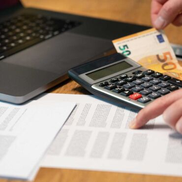 Hand hält 50-Euro-Schein neben Taschenrechner und Laptop – Förderung Barrierefreiheit: welche Mittel es gibt