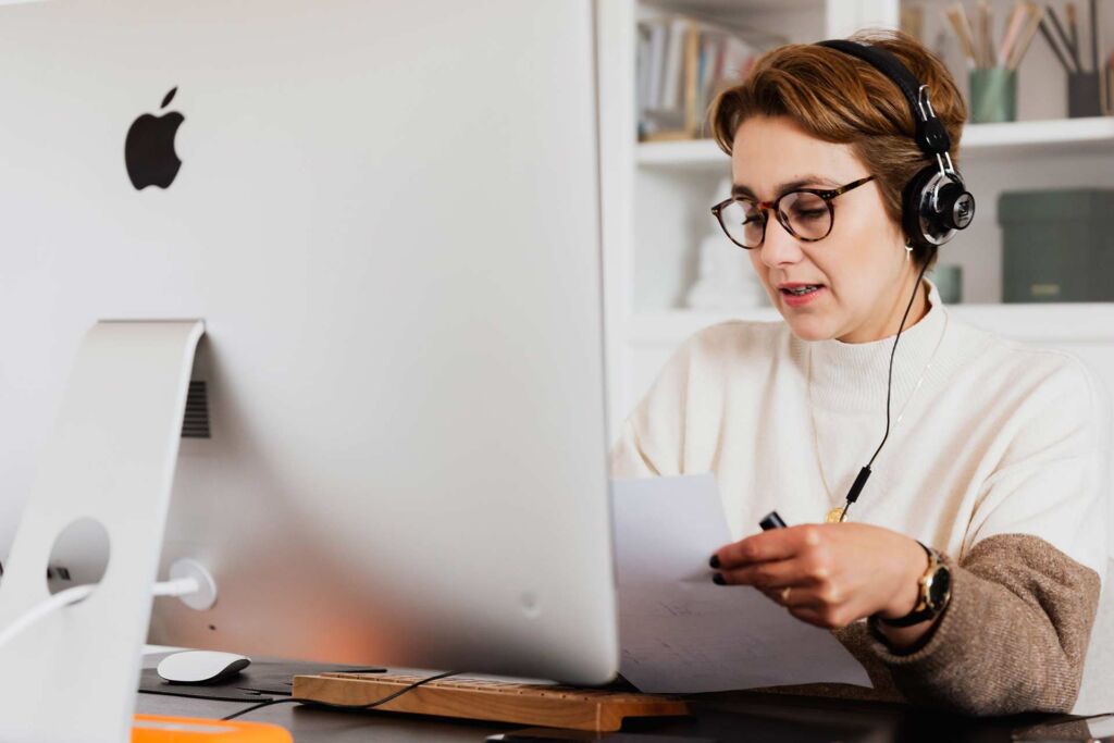 Person mit Kopfhörern am iMac hört Sprachausgabe und notiert sich Beobachtungen zur Screenreader-Nutzung