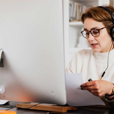 Person mit Kopfhörern am iMac hört Sprachausgabe und notiert sich Beobachtungen zur Screenreader-Nutzung