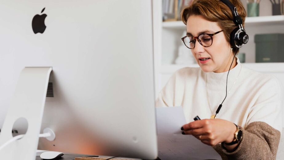 Person mit Kopfhörern am iMac hört Sprachausgabe und notiert sich Beobachtungen zur Screenreader-Nutzung