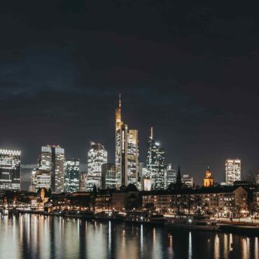 Beleuchtete Skyline einer Großstadt bei Nacht am Fluss – barrierefreie Smart City für digitale Teilhabe aller