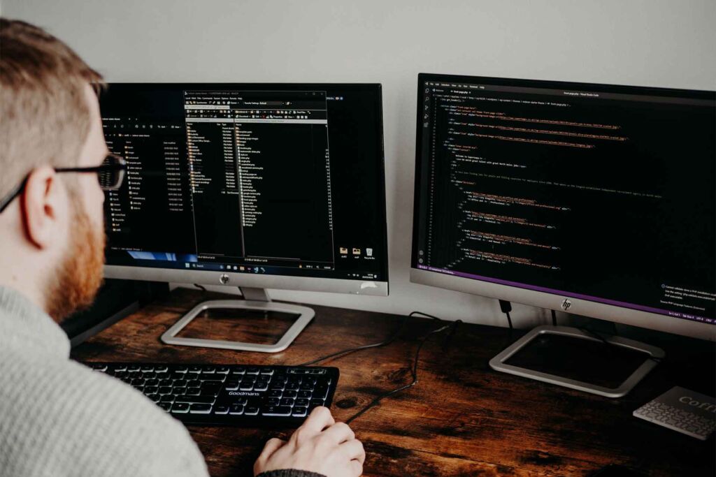 Programmierer schreibt HTML-Code an zwei Bildschirmen – barrierefreie Webentwicklung: semantisches HTML und ARIA