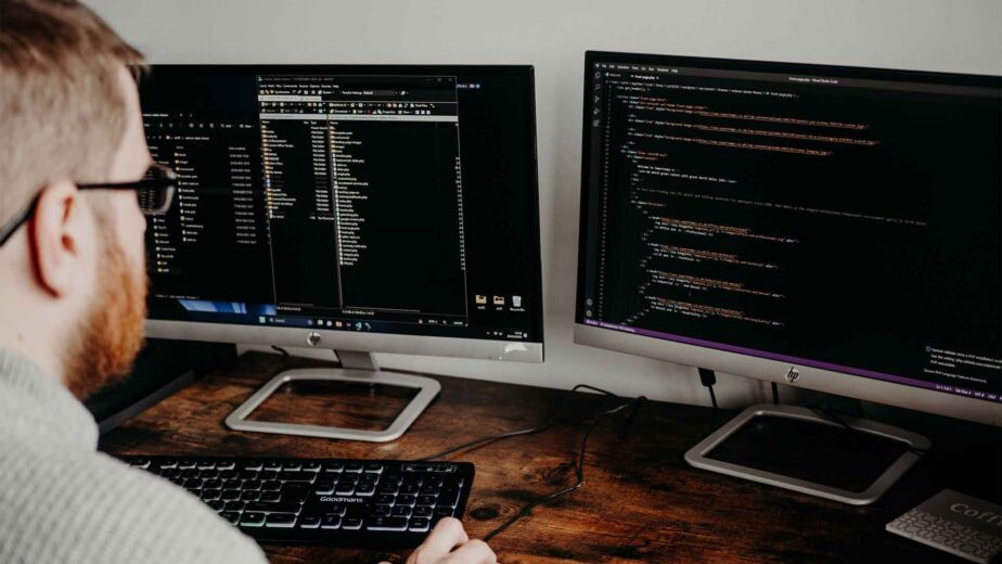 Programmierer schreibt HTML-Code an zwei Bildschirmen – barrierefreie Webentwicklung: semantisches HTML und ARIA
